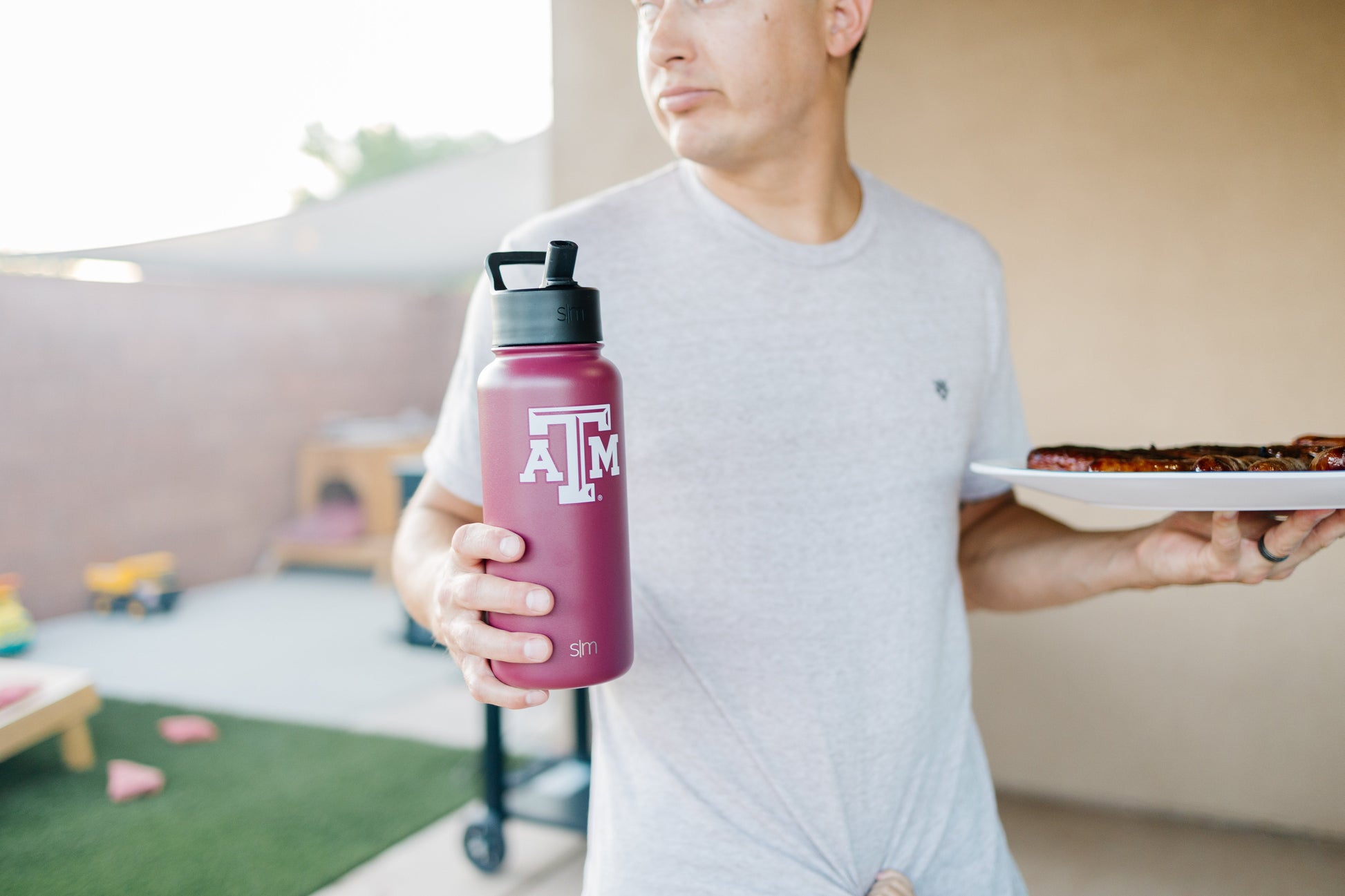 Deep burgundy water bottle held by man in light gray t-shirt against warm beige background