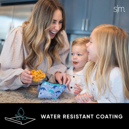 Woman in cream-colored sweater standing in modern kitchen with beige cabinetry, holding Ellie Snack Bag product package with bright yellow accent