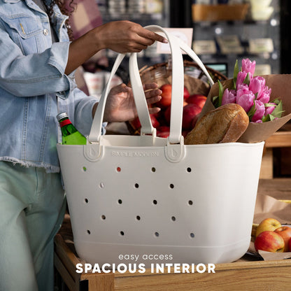 White Simple Modern tote bag filled with fresh groceries including pink tulips, bread, and apples, held by person in denim jacket at market counter. Spacious interior design with perforated ventilation.