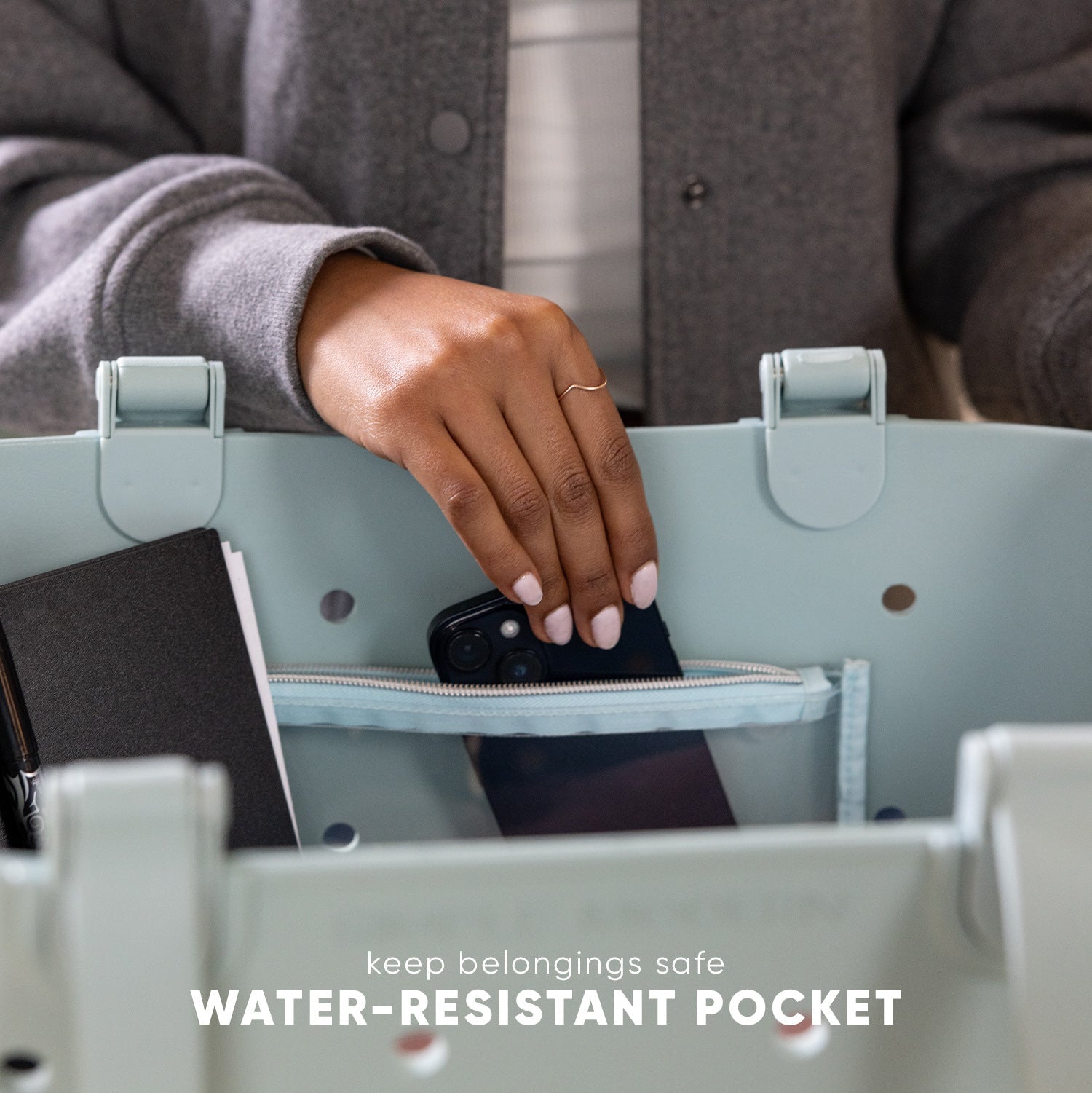 Person placing black smartphone into water-resistant pocket of light green Simple Modern Getaway Bag, demonstrating pocket functionality and storage capacity for keeping belongings safe.