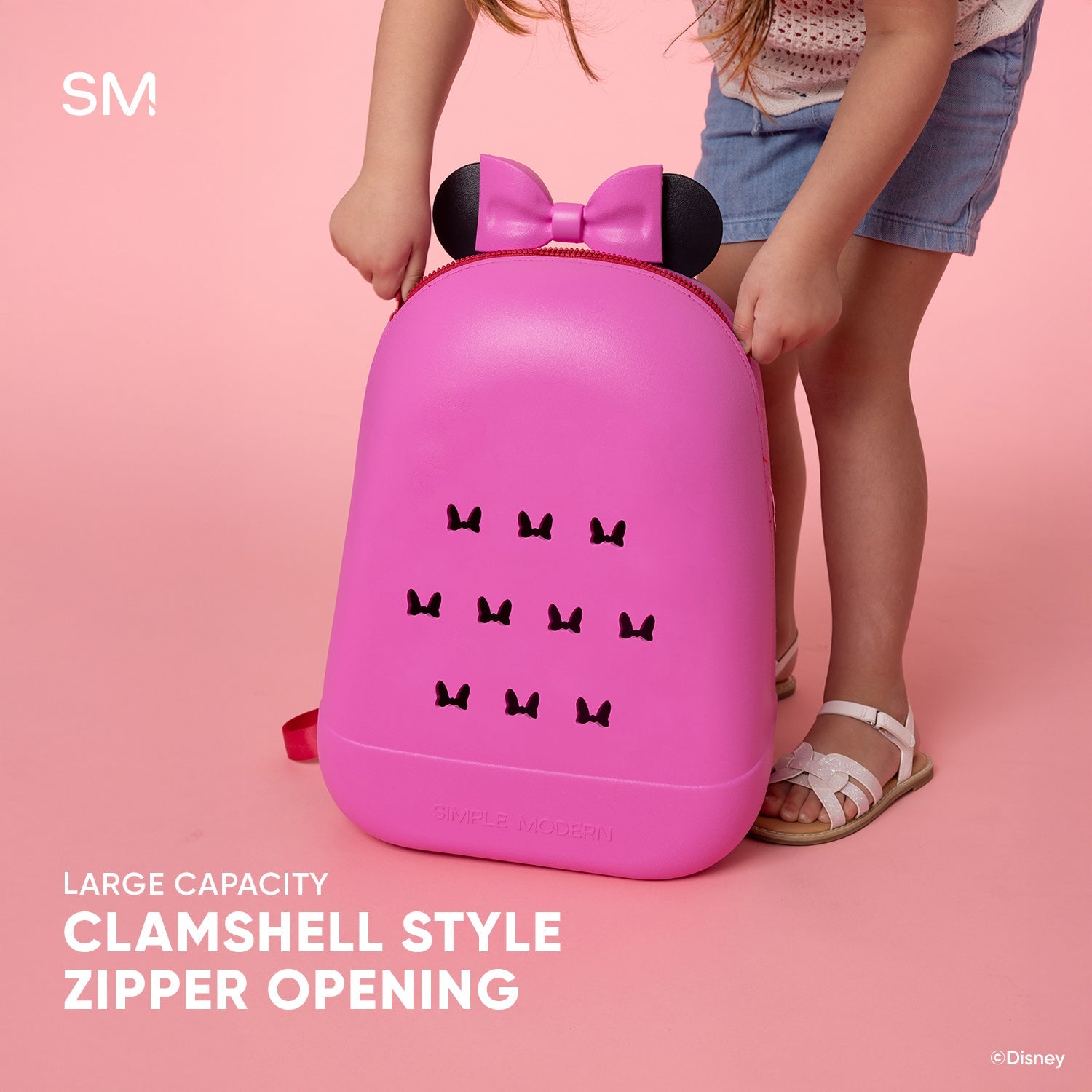 Hot pink Disney children's backpack with black bow-shaped ears and decorative bow icons, shown open against a soft pink background to display the clamshell opening design.
