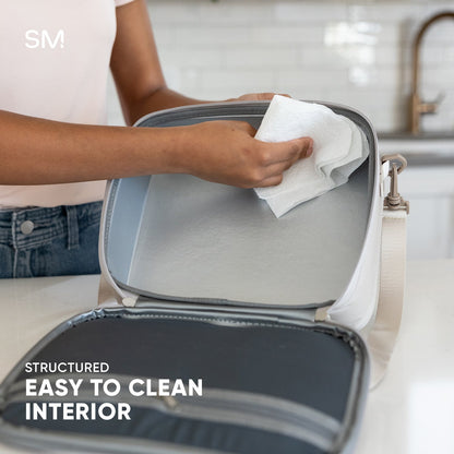 Light gray Simple Modern Hadley hardshell bag with white trim being wiped clean with a white paper towel, demonstrating easy-to-clean surface features.